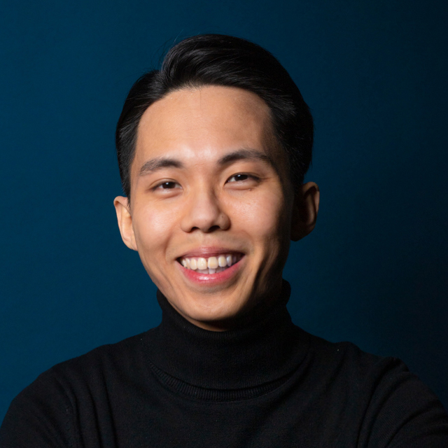 Portrait of a man with brown hair and glasses on a flat gray background.